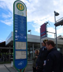 Großes Bushaltestellenschild mit Personen davor